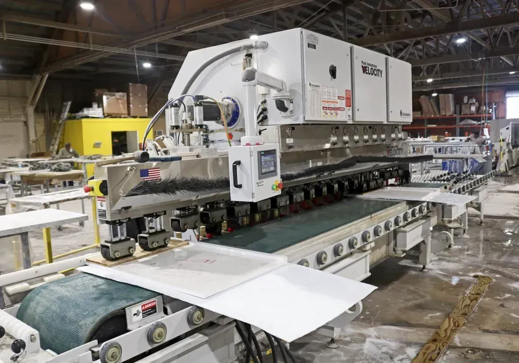 Large industrial machine processing white countertop material in a factory.