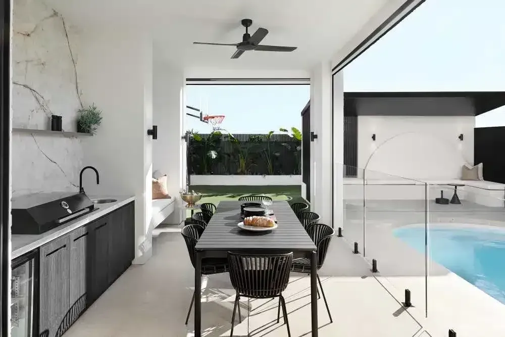 Outdoor dining area with black table and chairs, kitchen, and pool.