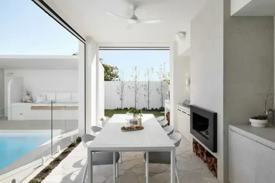 Outdoor dining area with a table, chairs, fireplace, and sliding glass doors overlooking a pool.
