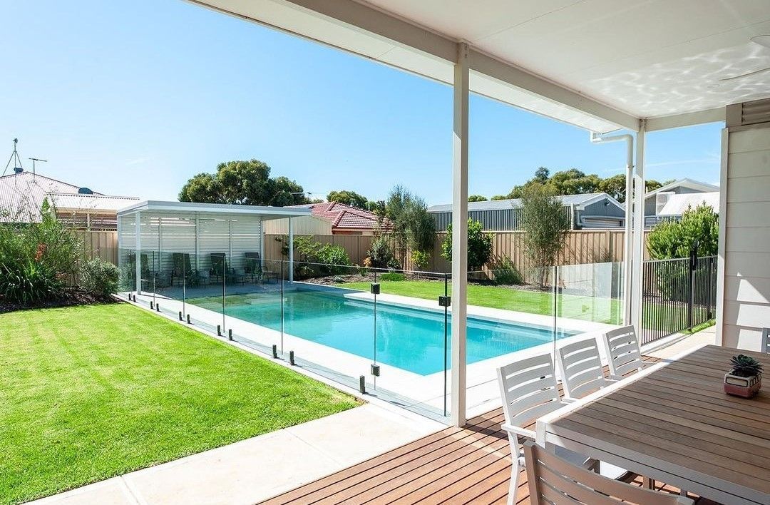 Backyard with pool, deck, dining table, and green lawn under a bright blue sky.