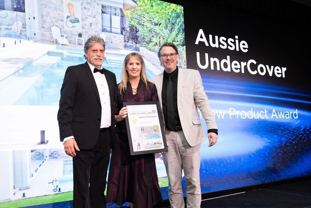 Three people holding an award, standing in front of a screen with 