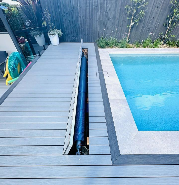 Pool with gray decking. A black pool cover is partially exposed; the pool has a light blue water surface.