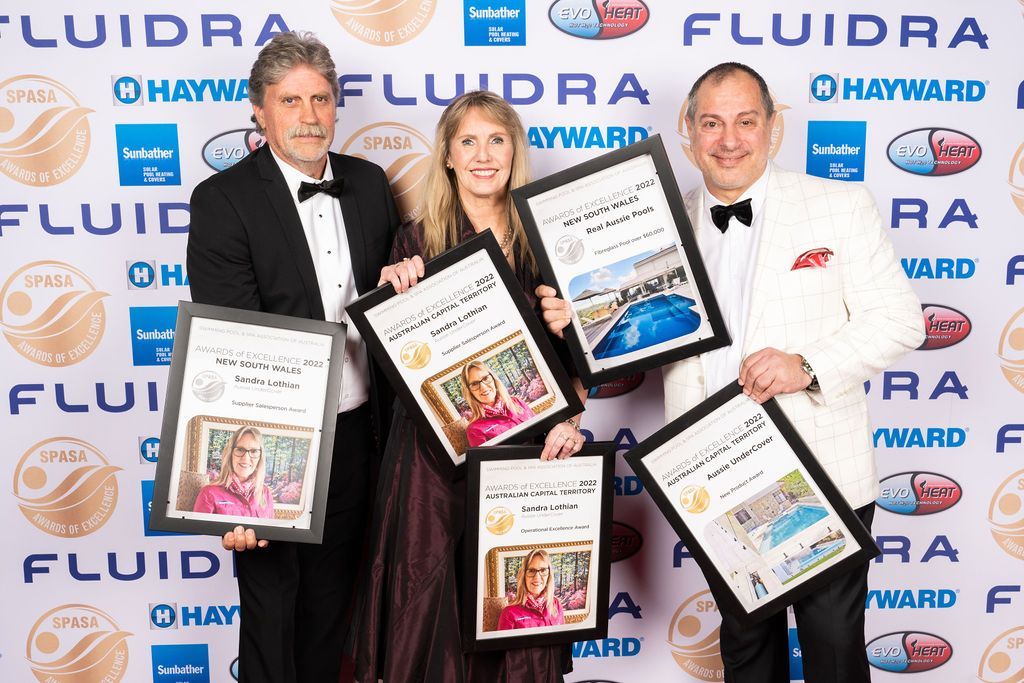 Three people holding framed awards in front of a backdrop with logos.