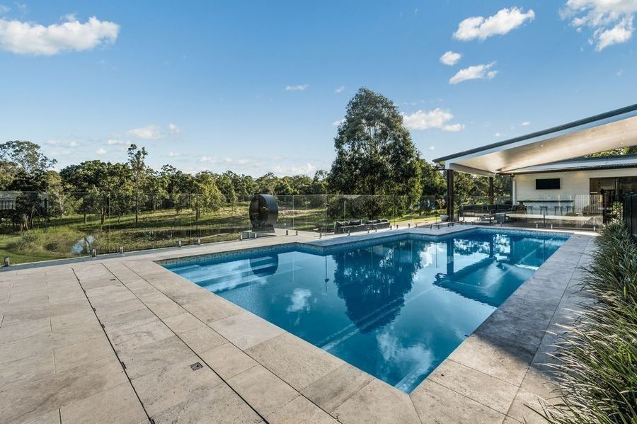 Swimming pool with blue water, concrete patio, and a covered patio area under a blue sky.
