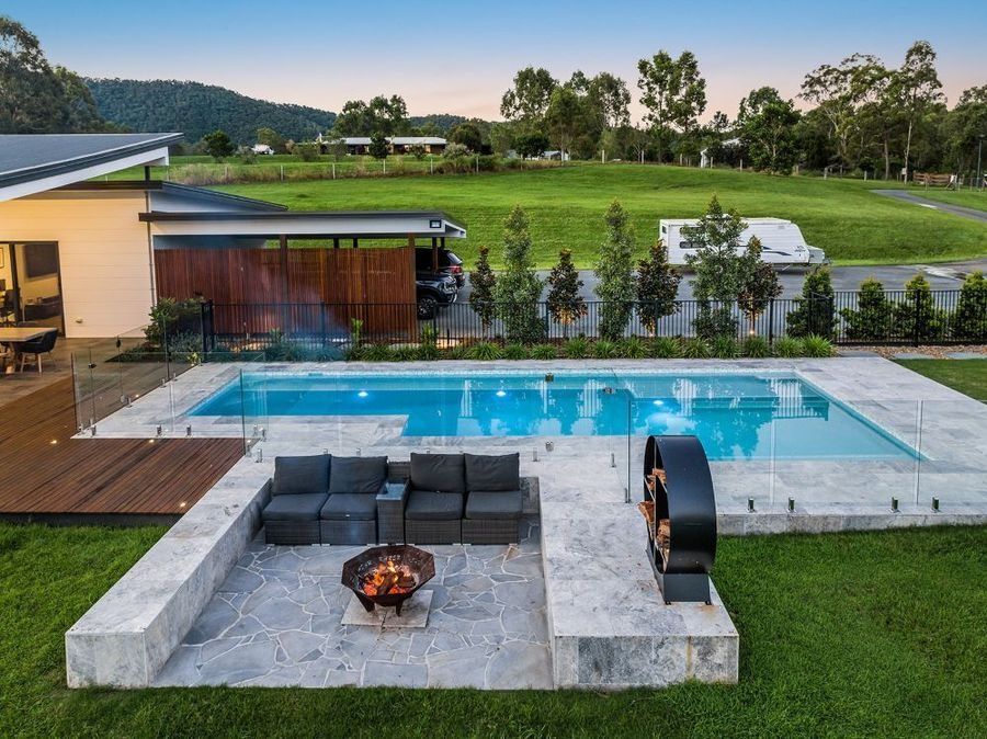 Pool area with lounge seating, fire pit, and a modern home in a grassy setting.