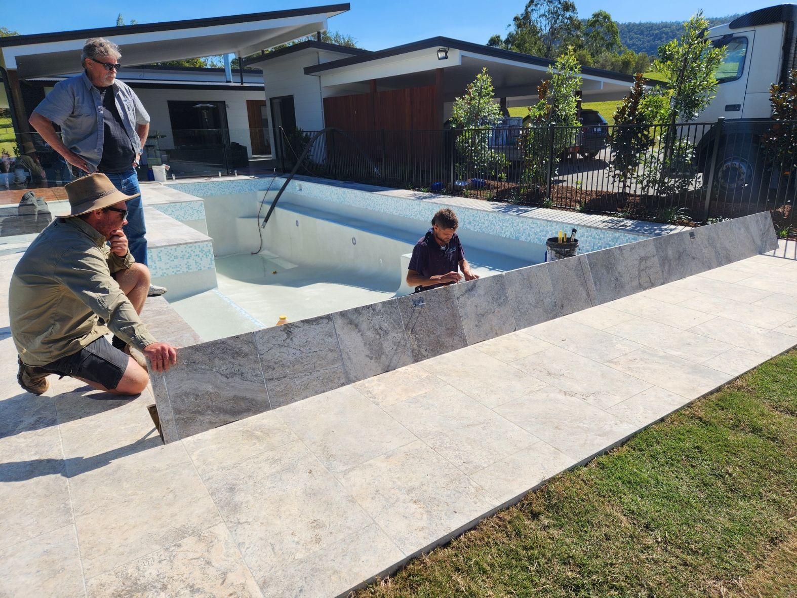 Three people installing a stone border around a swimming pool.