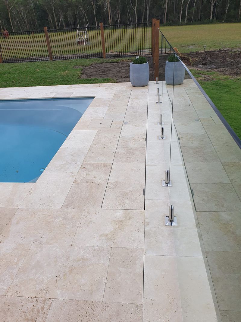 Poolside view with glass fence, concrete pavers, and potted plants.