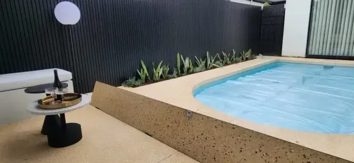 A small pool in a yard with a black fence, table, and plants.