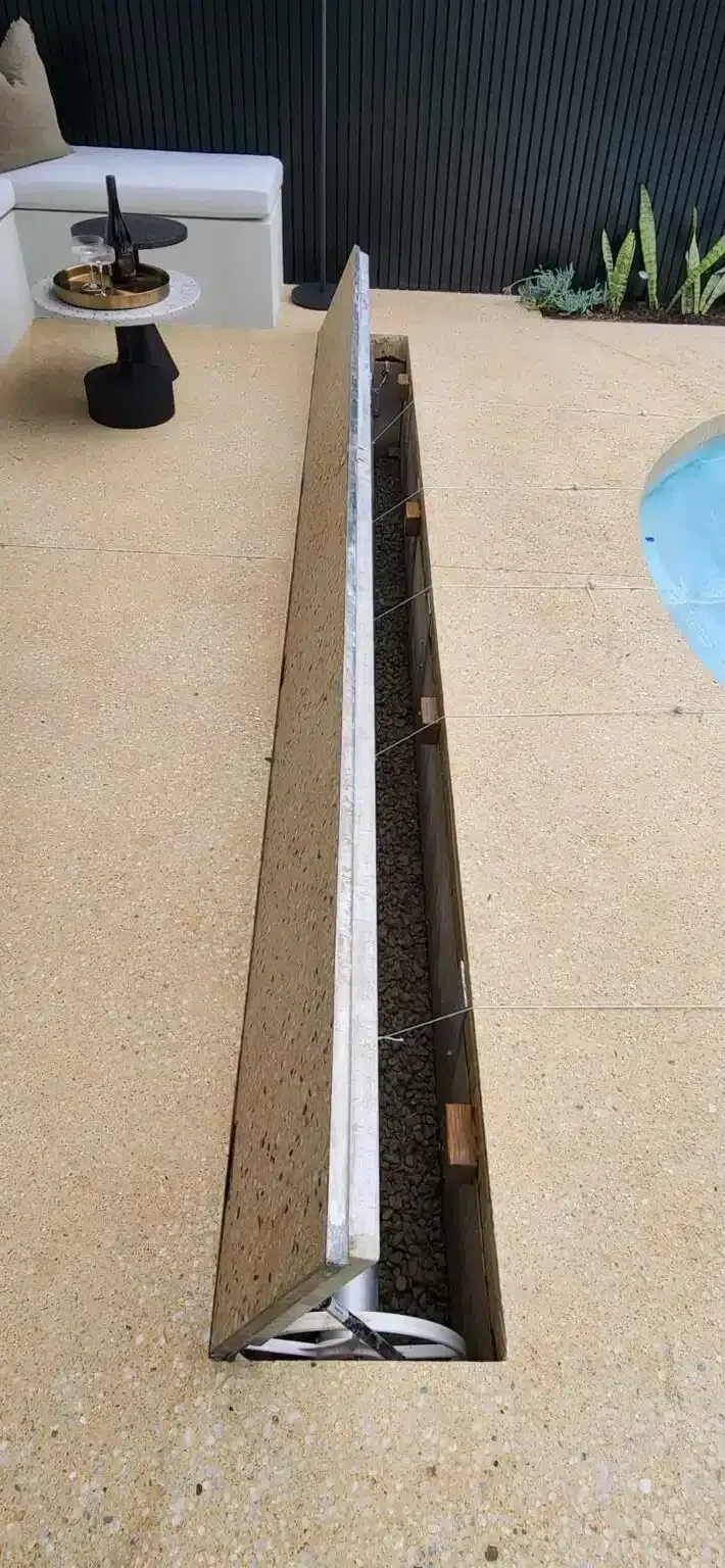 Open-lid drainage channel on a light-colored patio, next to a pool.