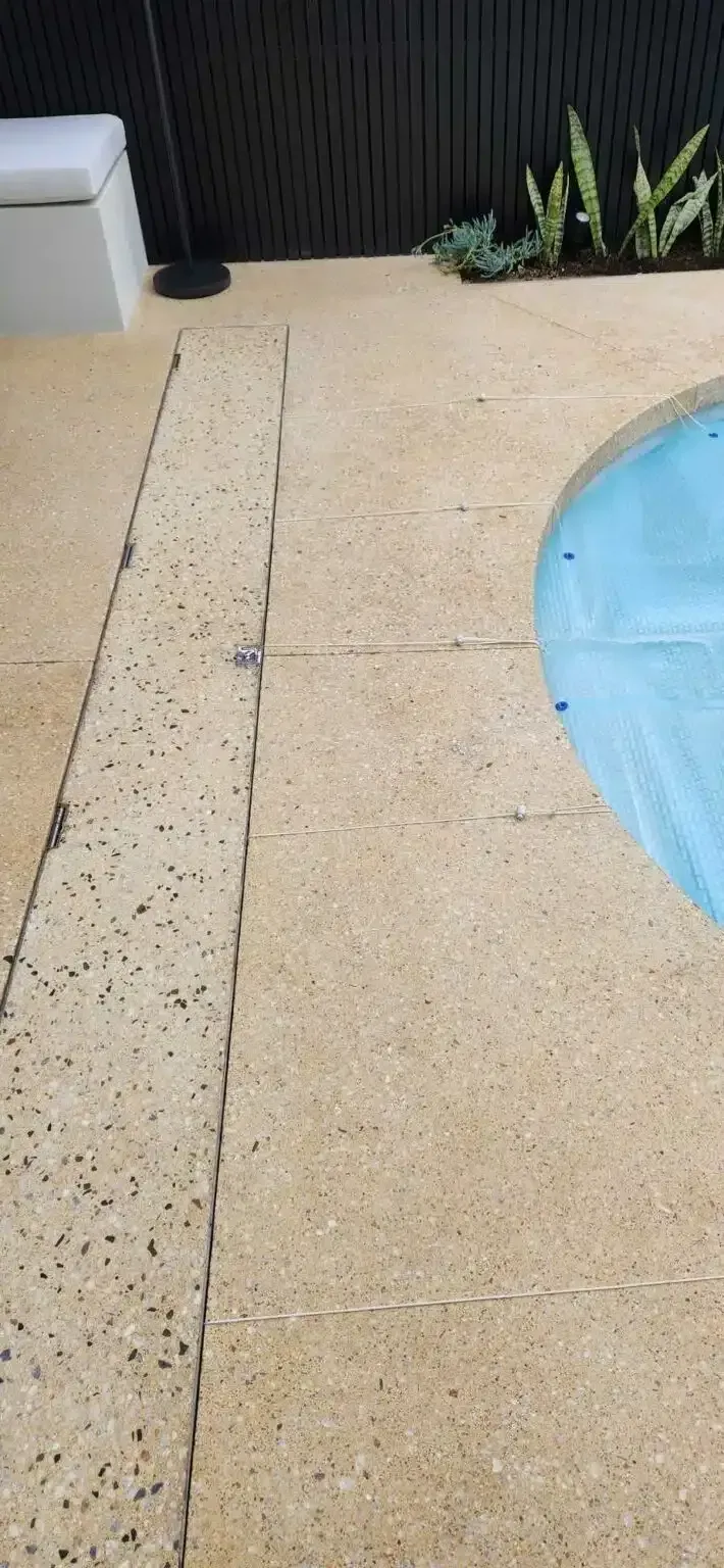 Poolside concrete, with light brown paving stones and a narrow, darker, inset drain. Blue water in pool.