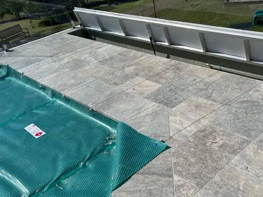 Green pool cover on a stone patio, with a raised white ledge.