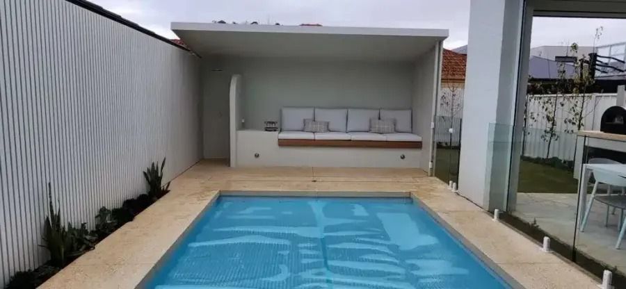 Small pool in a backyard with a seating area. White walls and a light blue pool.