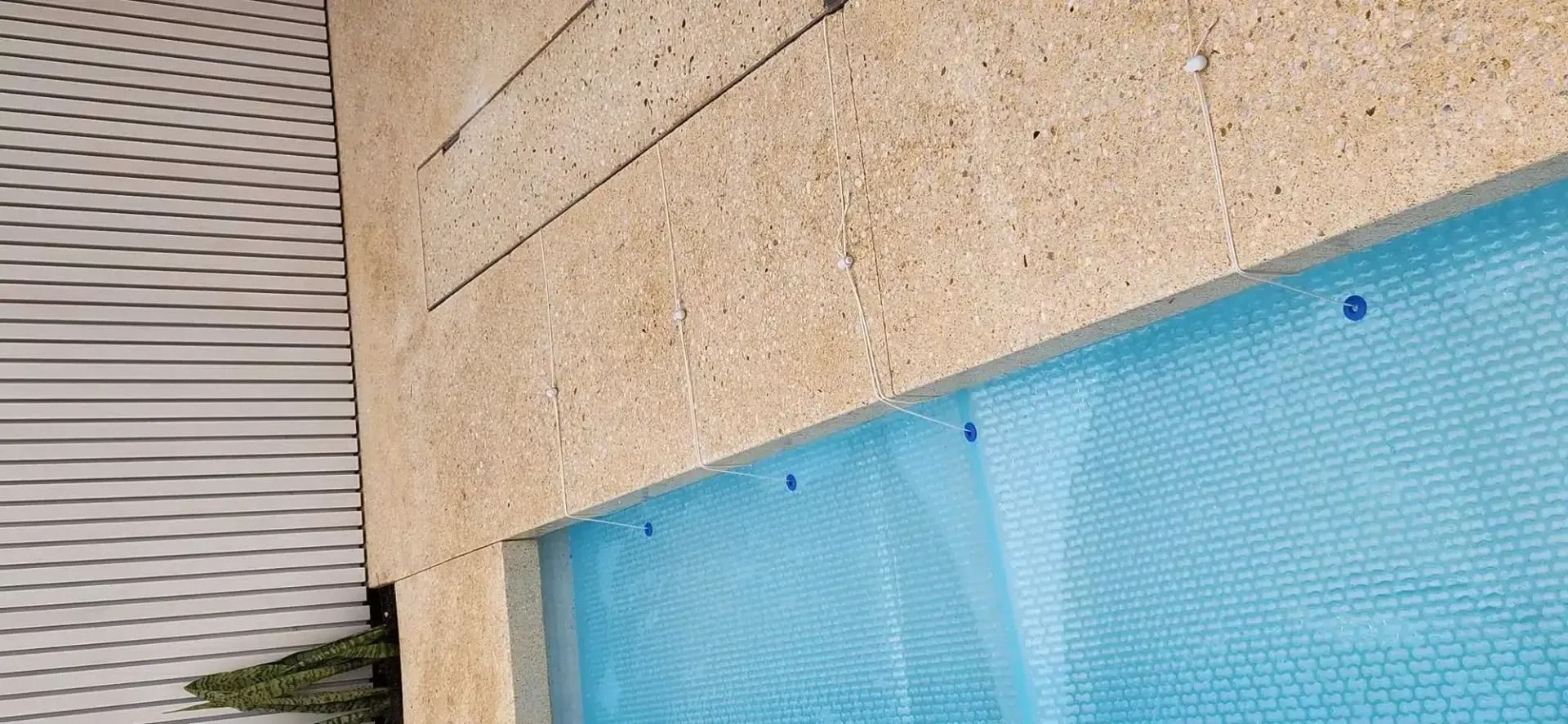 Close-up of a tan textured wall bordering a blue tarp-like material, possibly covering a pool.