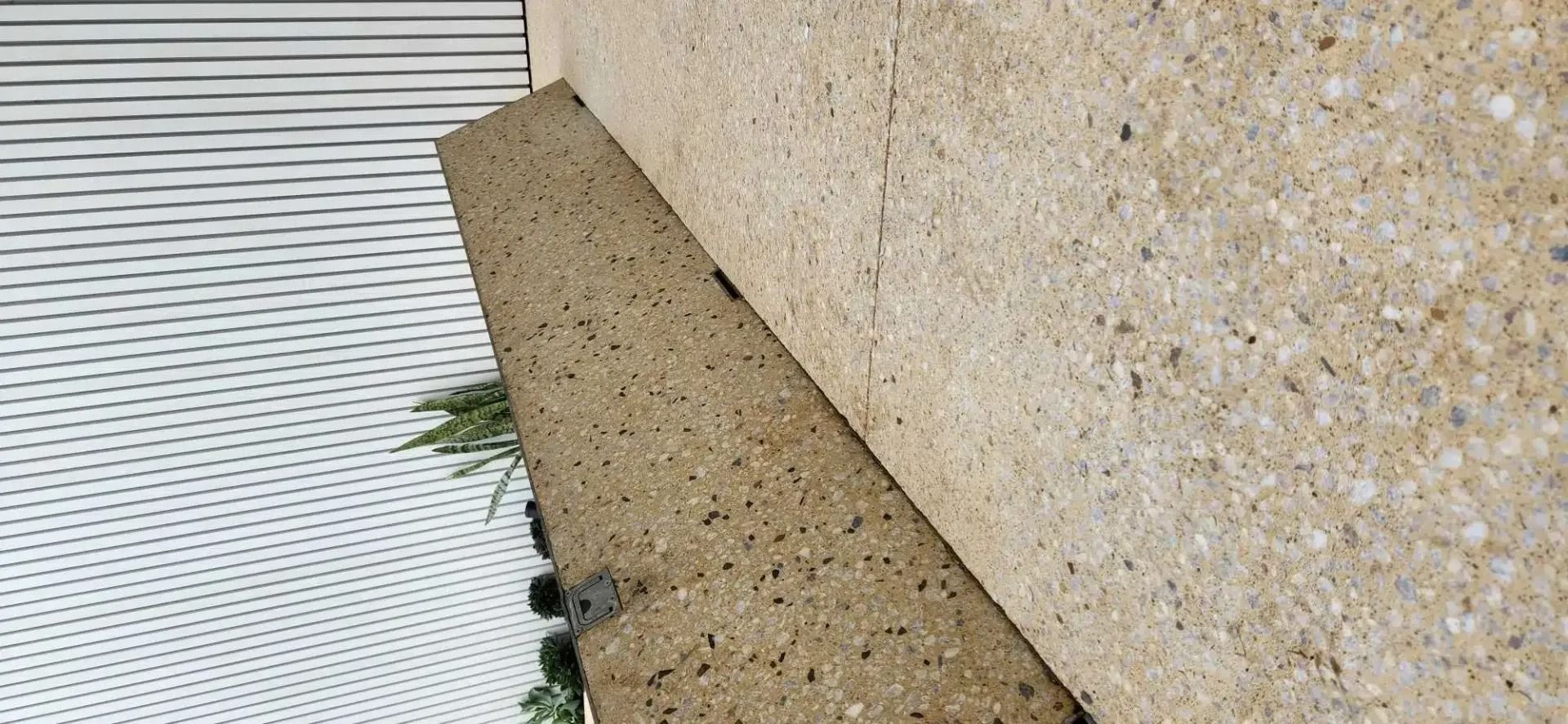Beige concrete walls meet a textured stone ledge, with white siding visible to the left.
