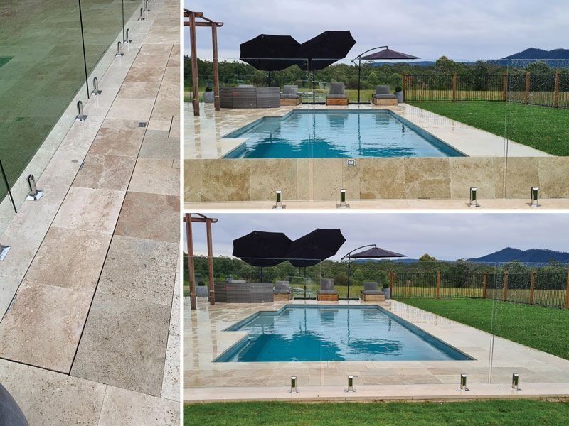 Swimming pool with glass fencing, umbrella, and stone patio. Green grass and hills in the background.