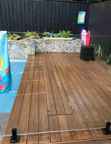 Wooden deck beside a pool with an inflatable pool toy and stone wall in the background.