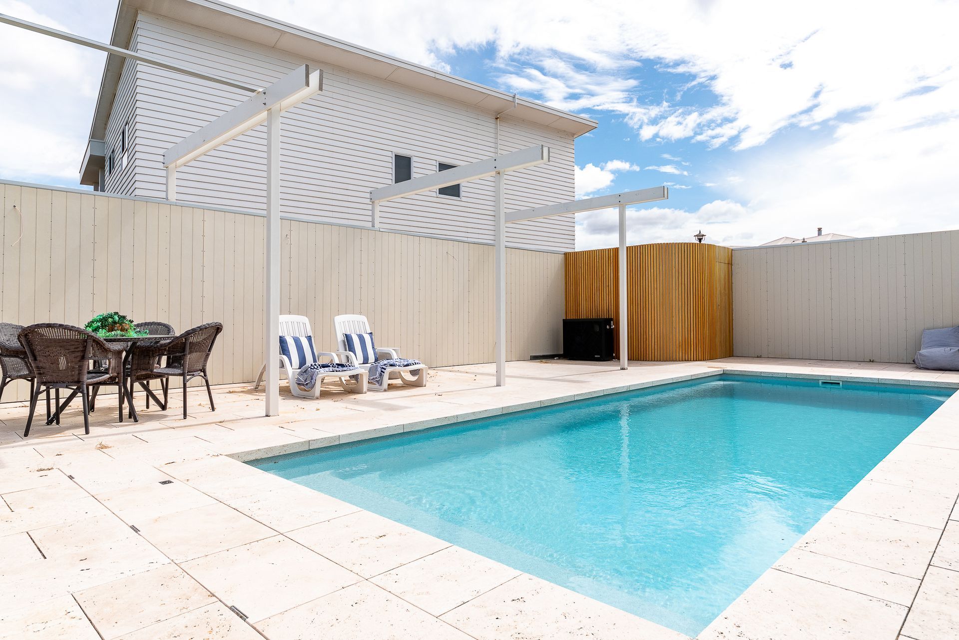 Pool with blue water and cover, glass fence, grass and ocean in background.