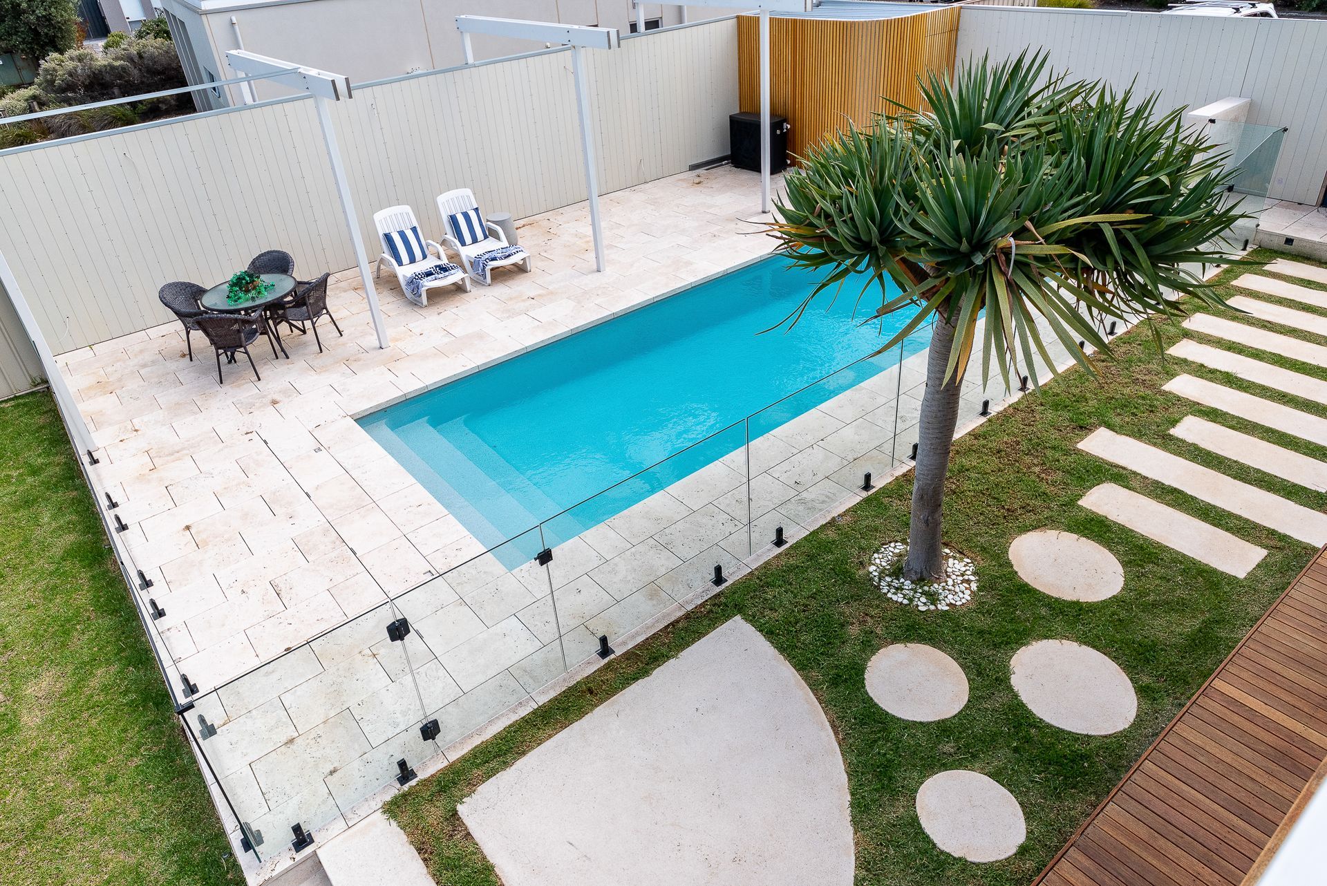 Backyard with swimming pool, lounge chairs, dining set, and landscaping; sunny day.