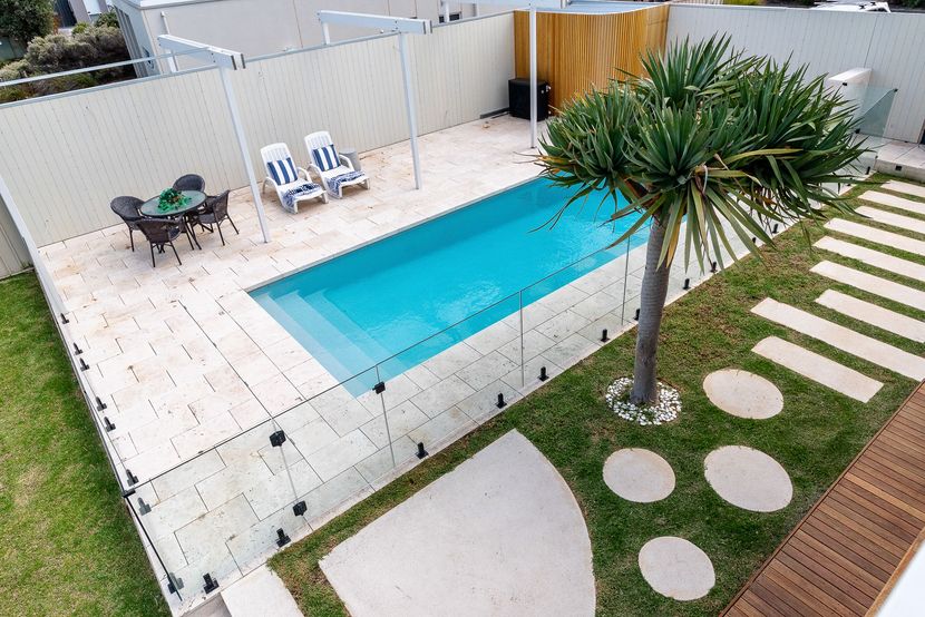 Backyard with swimming pool, lounge chairs, dining set, and landscaping; sunny day.
