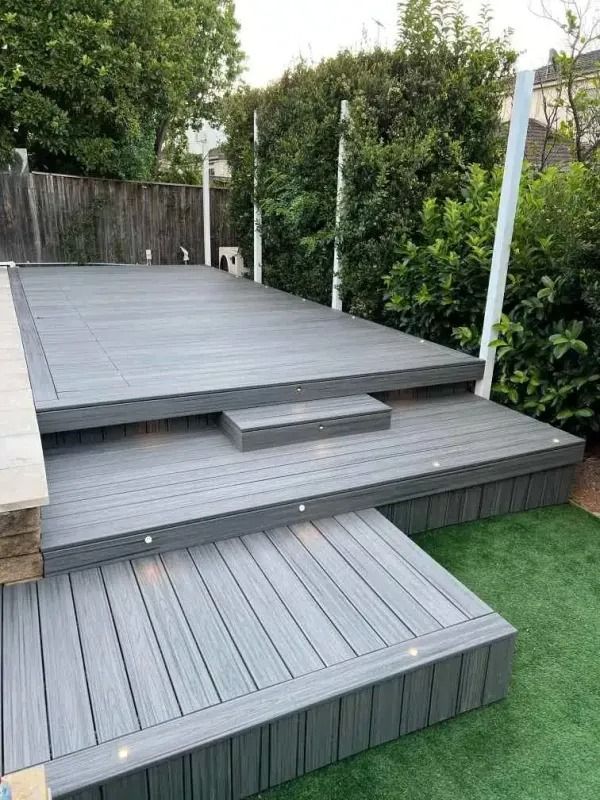 Grey composite deck with three levels and built-in lighting in a backyard setting.