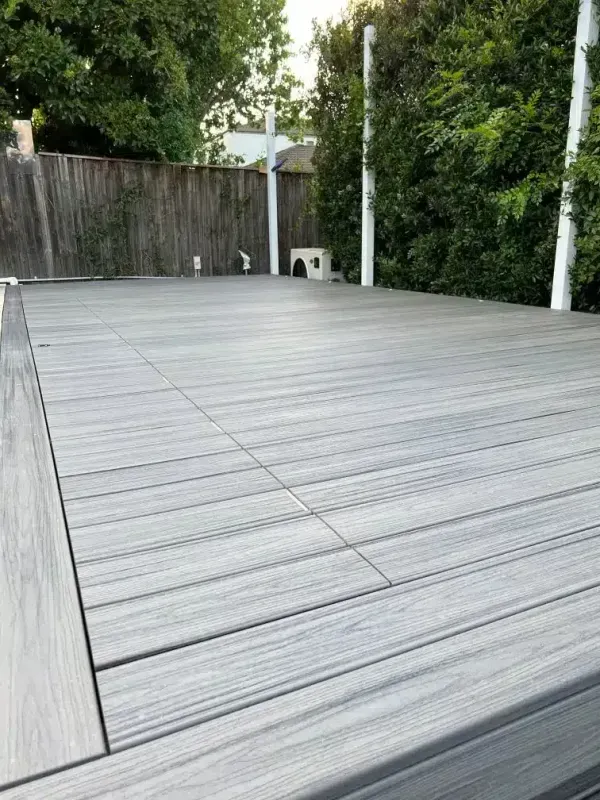 Gray composite deck with a wooden fence and trees in the background.