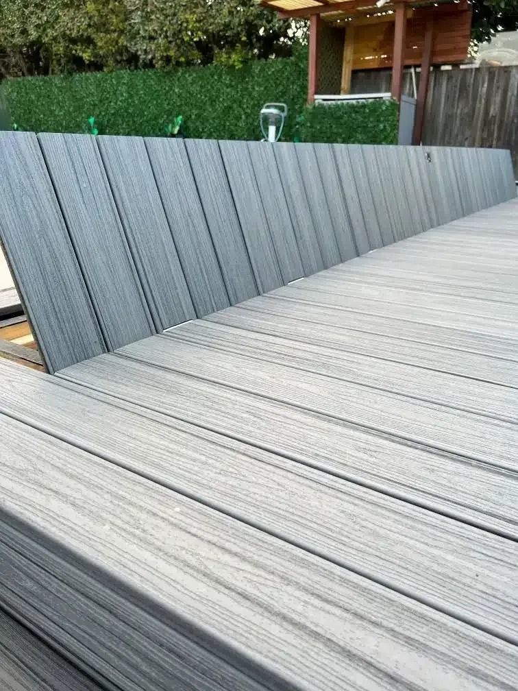 Gray composite deck with matching built-in bench, with a grass hill and wooden structure in the background.