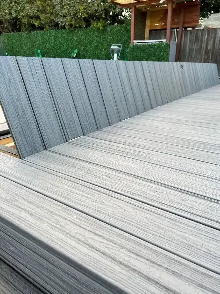 Gray composite deck with a sloped backrest, leading to a green hedge and small wooden structure.