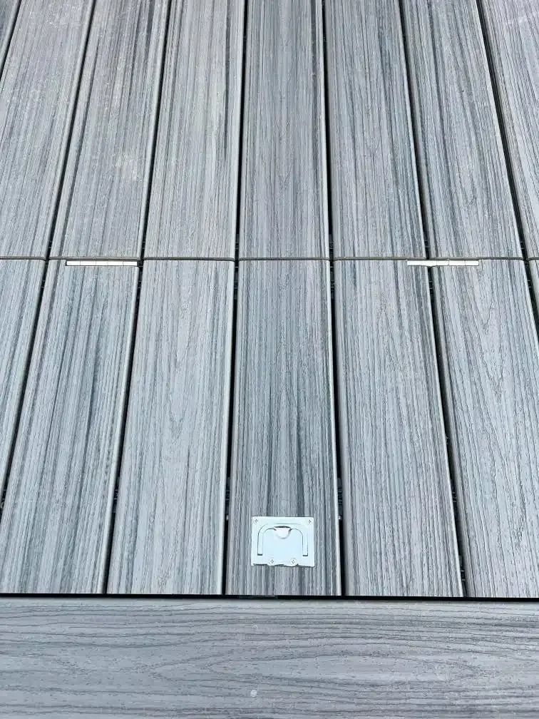 Gray wooden deck with rectangular access panel and recessed lighting.