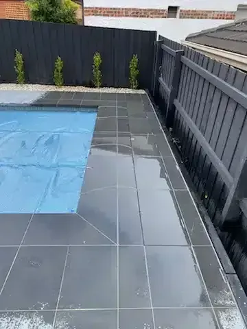 Dark gray tiled pool surround next to a dark gray wooden fence; blue pool cover partially visible.