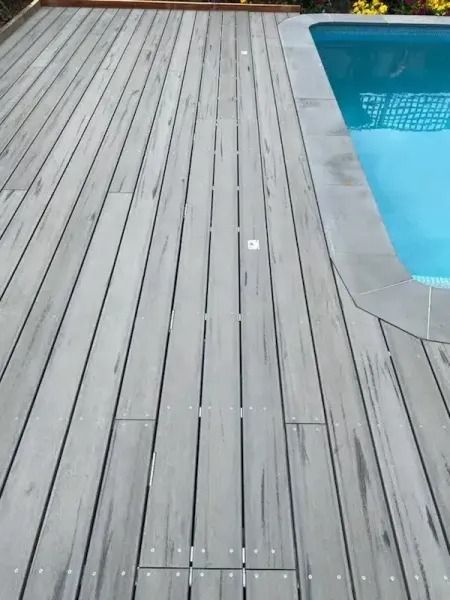 Gray wooden deck next to a pool with light blue water.