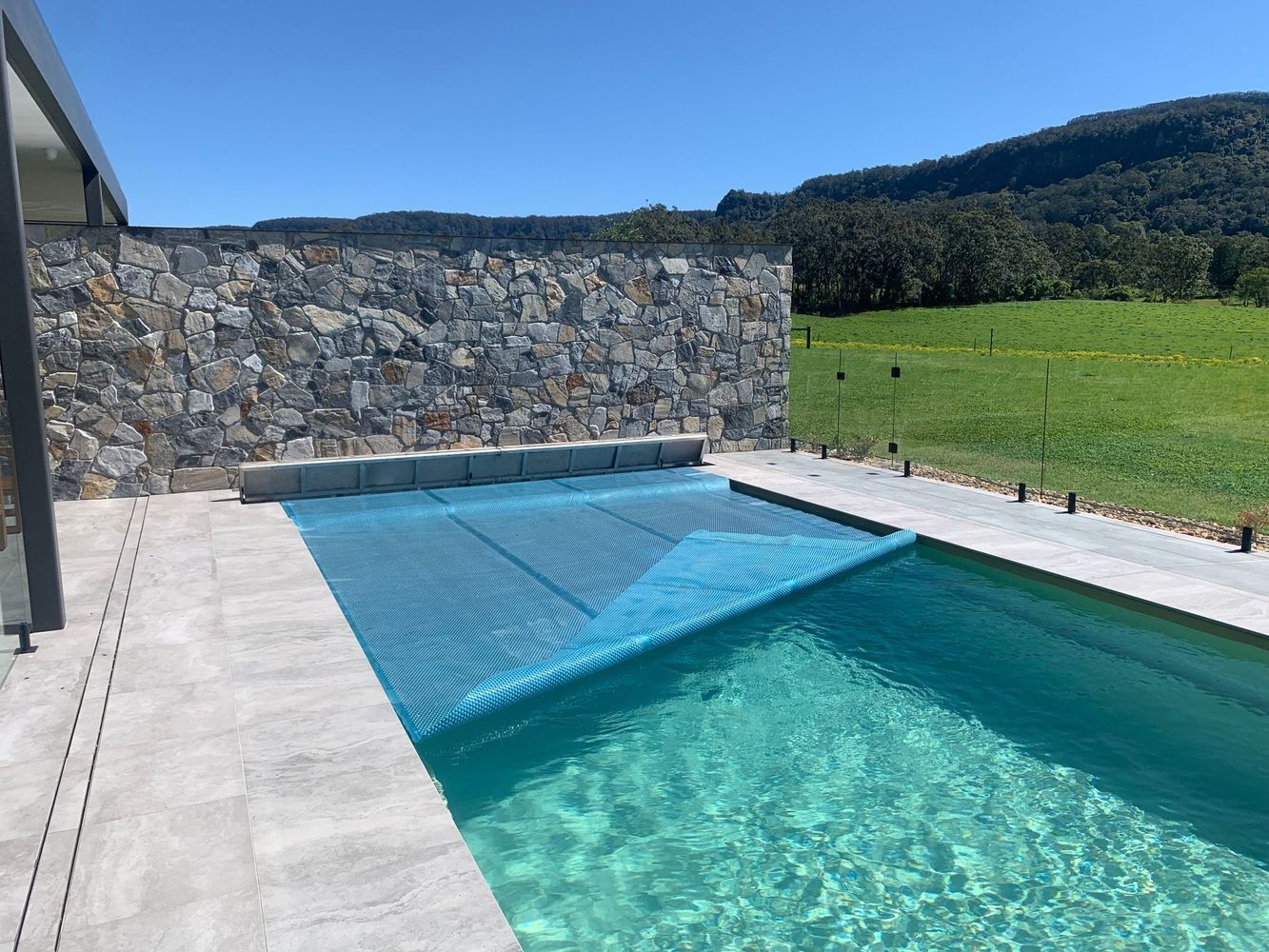 Overhead view of rectangular pool with light blue water, surrounded by light-colored concrete and green grass.