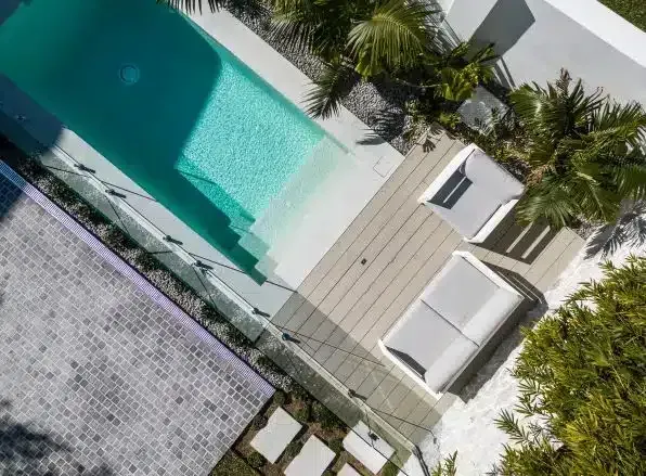 Overhead view of a white rectangular pool with steps, lounge chairs, and tropical landscaping.