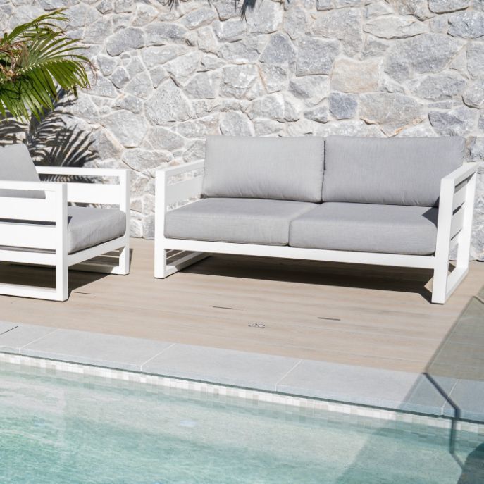 White outdoor sofa set with gray cushions by a pool against a stone wall.