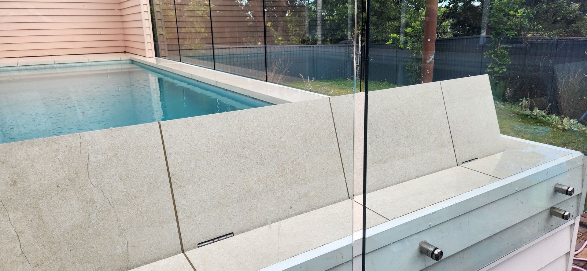 Pool with blue water and cover, glass fence, grass and ocean in background.