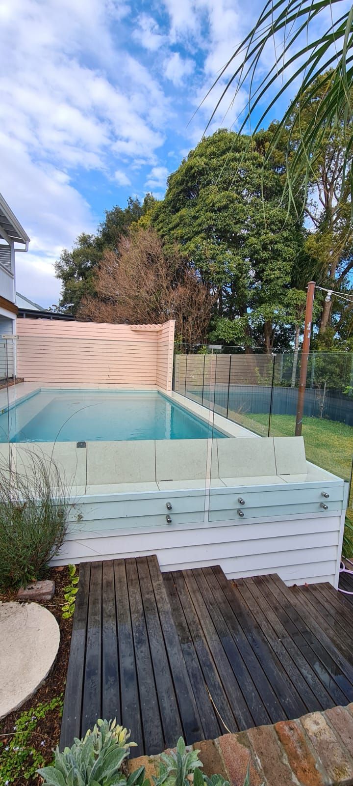 Wooden deck with black chairs and lush greenery by a pool.