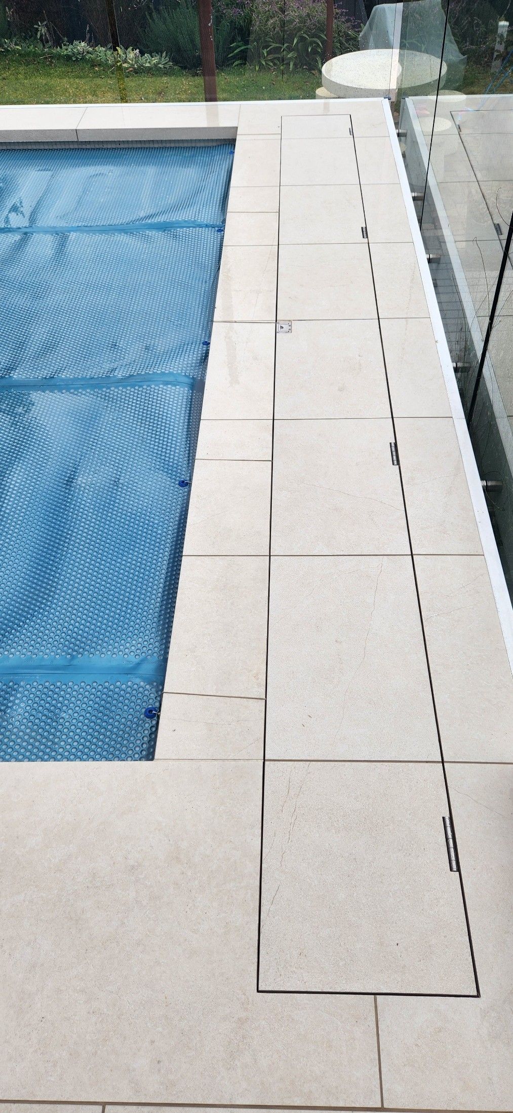 Overhead view of a rectangular turquoise pool, pergola, and green lawn.