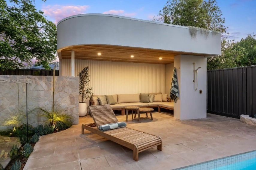 Poolside cabana with lounge seating, wooden deck chair, and outdoor shower.