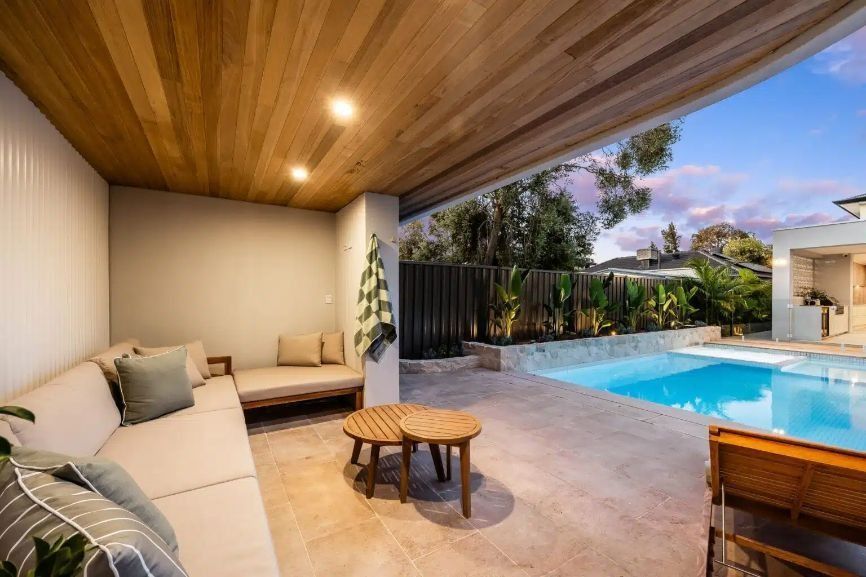 Outdoor lounge area with a pool. Beige couches, wooden ceiling, and pool with blue water.