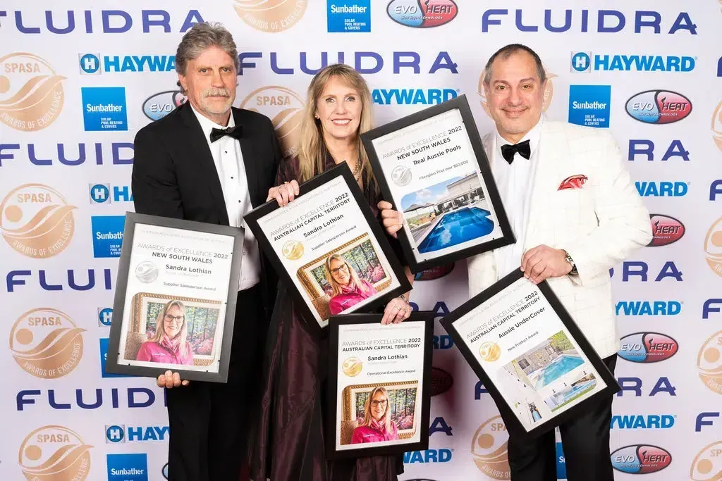 Three people holding framed awards in front of a backdrop with logos.