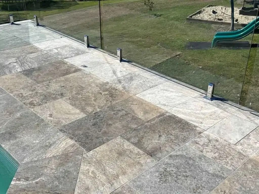 Stone patio with glass fence overlooking a grassy area with a slide.