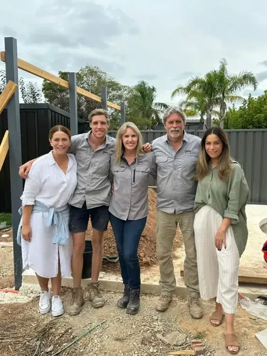 Group of five people pose for a photo in front of a construction site; overcast skies.
