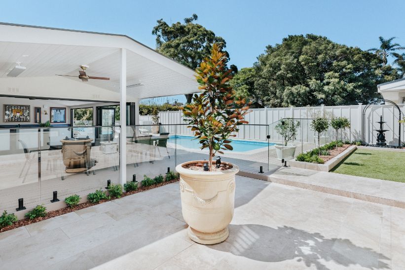 Patio with a potted tree, pool, and white covered area. Sunny day.