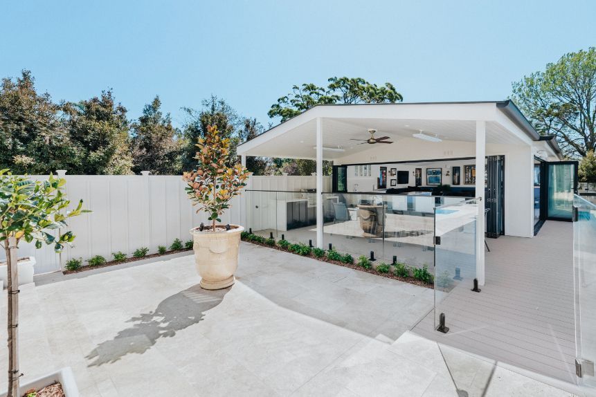 Outdoor patio with a white canopy, kitchen, glass railing, and potted trees.