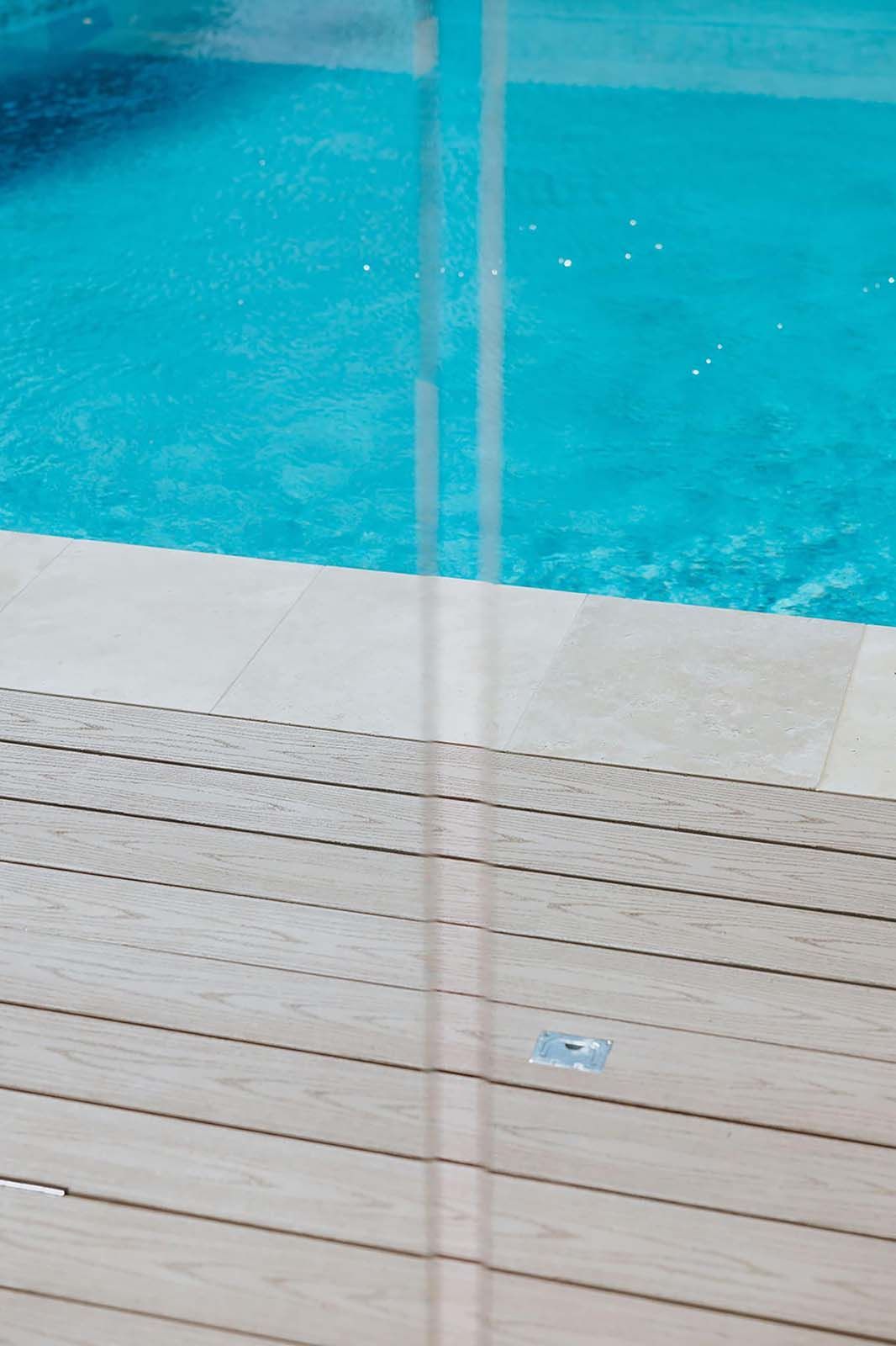 Blue pool water and light brown wooden deck.