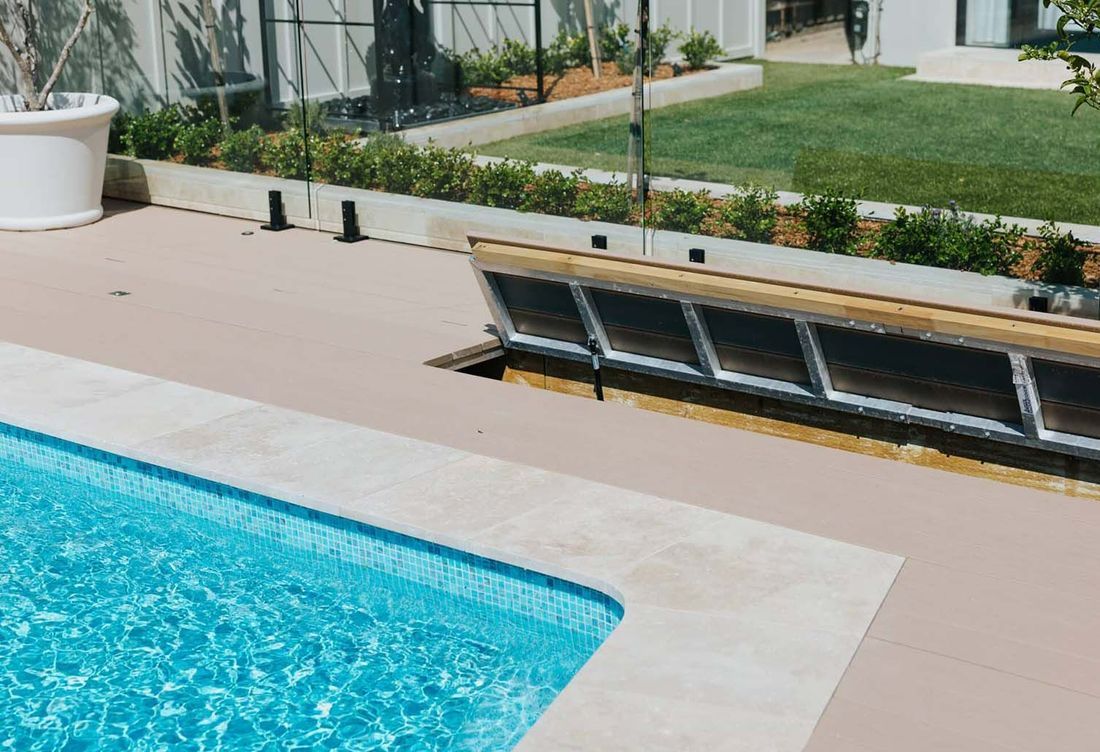 Pool with light-colored coping, surrounded by a light-brown patio. Hidden pool cover near a grassy area.