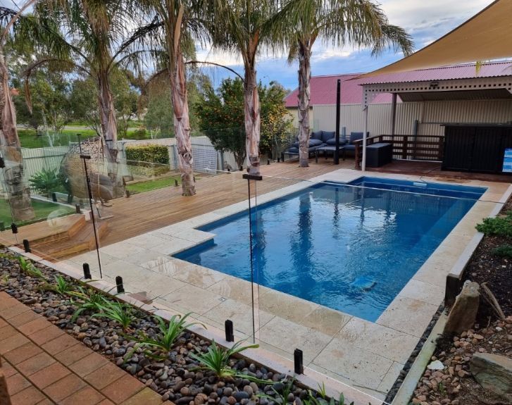 Pool with blue water and surrounding stone patio, palms, and seating area.