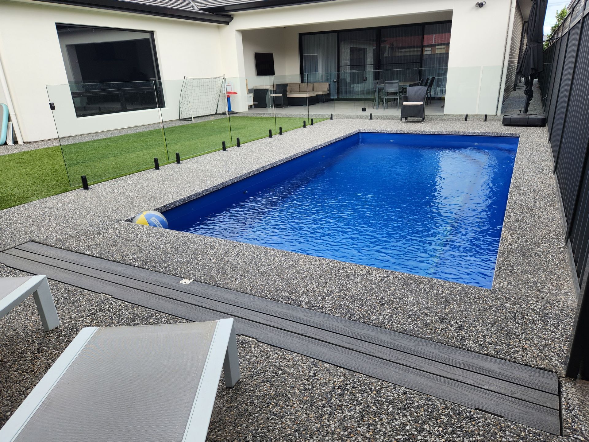 Overhead view of a rectangular turquoise pool, pergola, and green lawn.