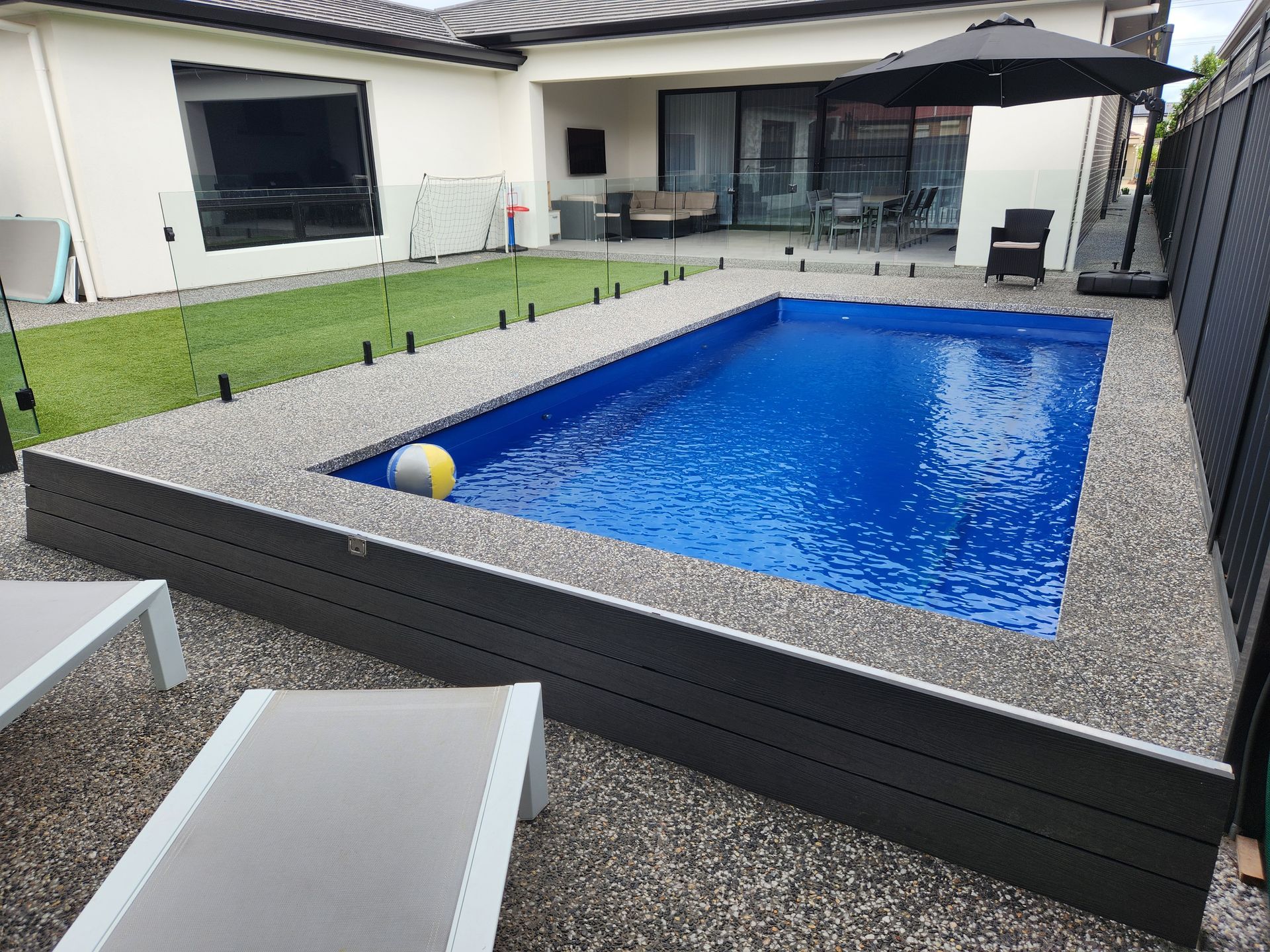 Overhead view of a rectangular turquoise pool, pergola, and green lawn.