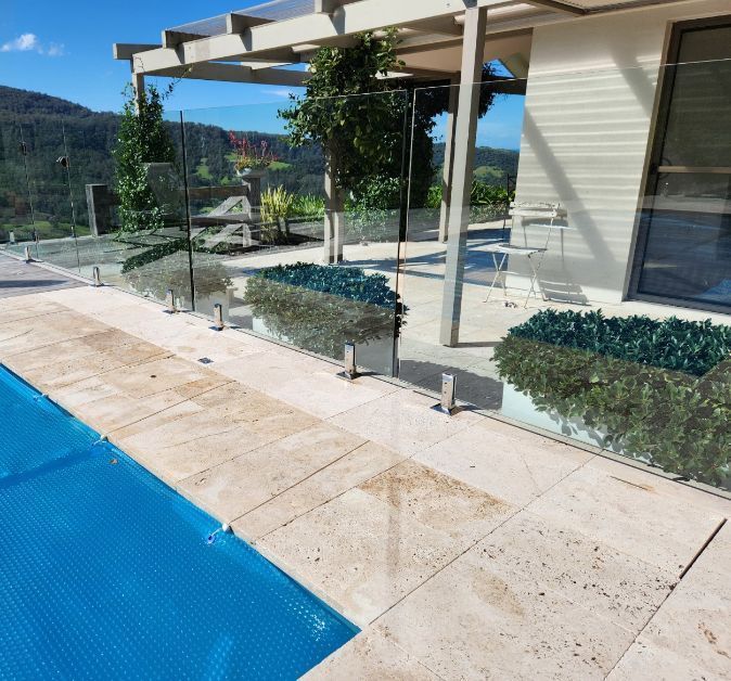 Swimming pool with glass fence, patio, and hillside view.