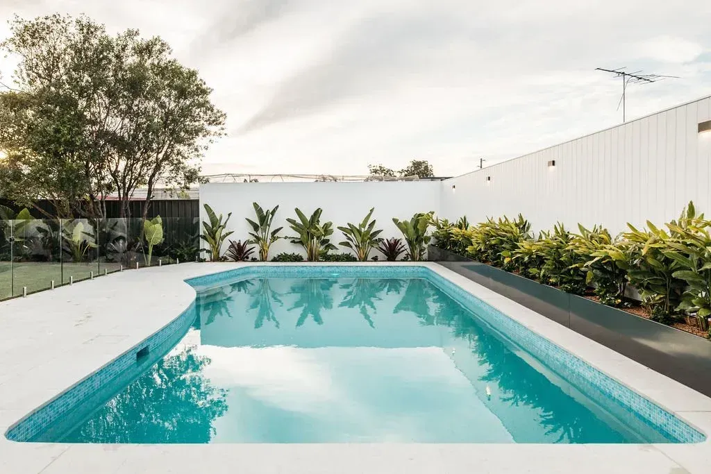 Rectangular swimming pool with turquoise water, surrounded by white decking and greenery.